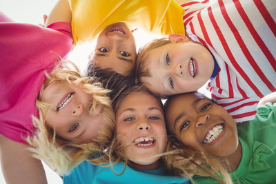 Fünf Kinder stecken in einem Kreis die Köpfe zusammen, so dass man ihre lachenden Gesichter sieht.