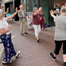 Eine Gruppe älterer Menschen mach mitten in der Stadt Bewegungsübungen.