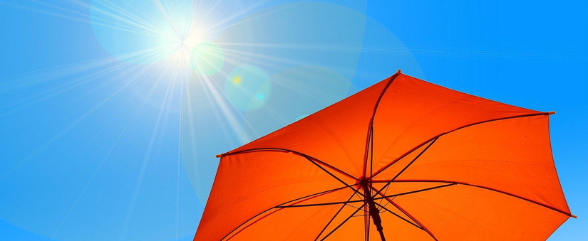 Ausschnitt eines roten Sonnenschirms vor einem blauen Himmel mit Sonne.