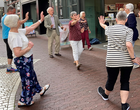 Eine Gruppe älterer Menschen mach mitten in der Stadt Bewegungsübungen.