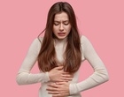 Eine junge Frau hält sich mit beiden Händen den Bauch. Symbolbild für Bauchschmerzen.
