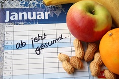 Auf einem Kalenderblatt liegen Nüsse und Obst. Symbolbild für gute Vorsätze.