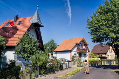 Eine Frau spaziert auf einer Straße mit alten Häusern und grünen Vorgärten