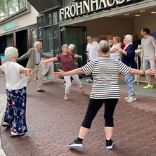 Eine Gruppe älterer Menschen mach mitten in der Stadt Bewegungsübungen.