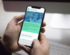 Zwei Hände halten ein Smartphone, auf dem die Website postcovil-rlp.de zu sehen ist.