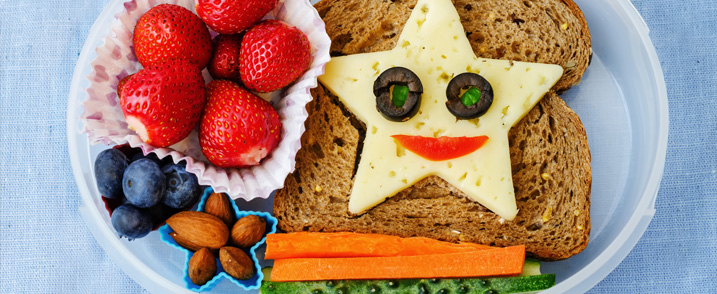 Abgebildet sind gesunde Lebensmittel: Erdbeeren, Blaubeeren, Nüsse, Karottenstifte, ein Vollkornbrot mit einer Käsescheibe in Sternform.